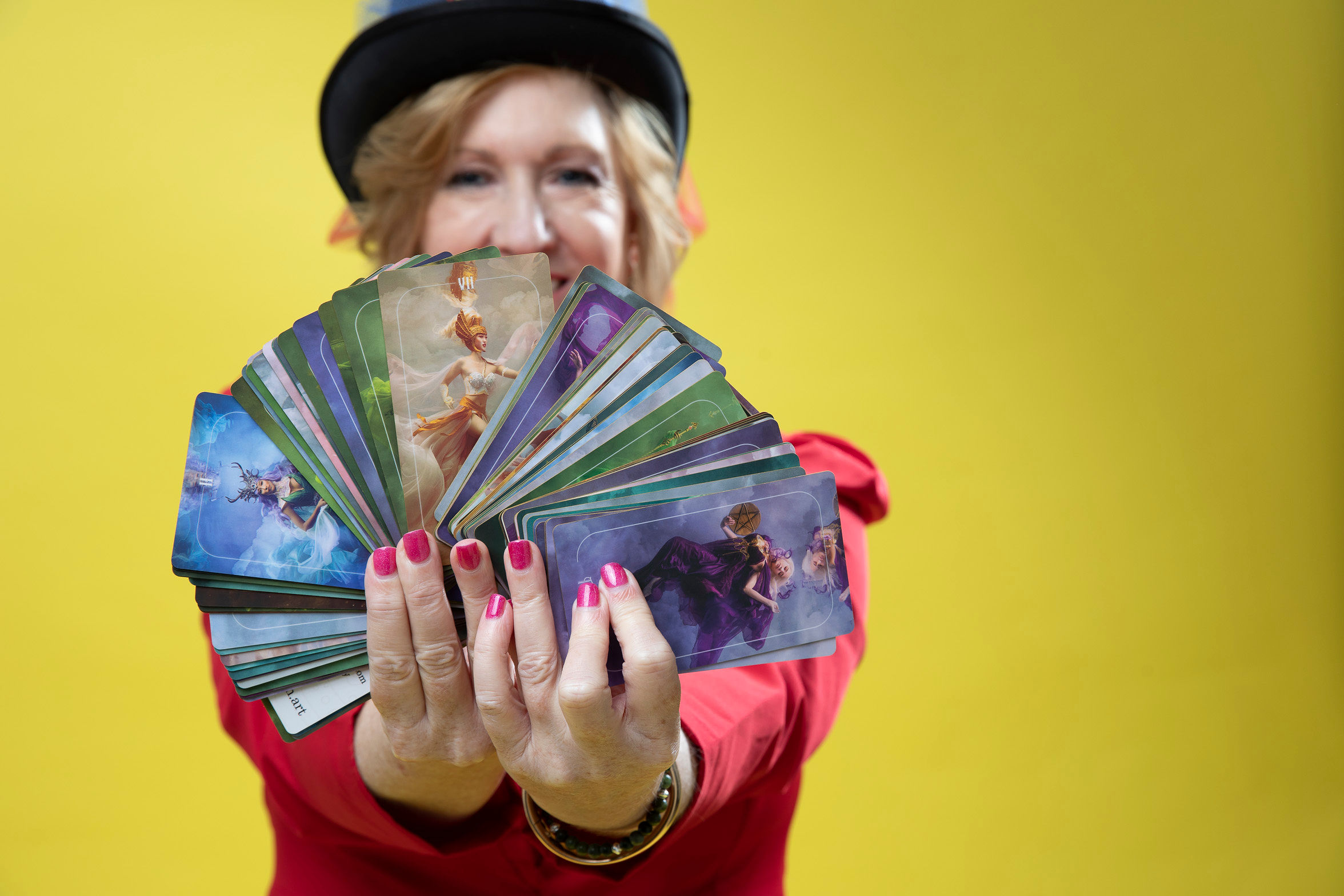 Elizabeth Toller holding a fan of colorful tarot cards against a bright yellow background, creating a bold fine art portrait focused on creativity and intuition.