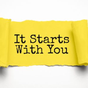 IT STARTS WITH YOU. words. text on yellow paper on torn paper background
